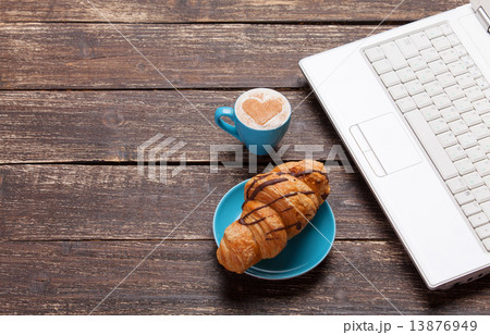 Croissant and cup of coffee with laptop on wooden table. Croissant and cup of coffee with laptop on wooden table. 13876949