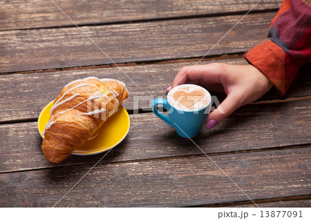 Female hands holding cup of coffee with croissant on wooden tabl 13877091