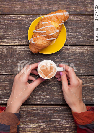 Female hands with cup of coffee and croissant on wooden table. Female hands with cup of coffee and croissant on wooden table. 13877408