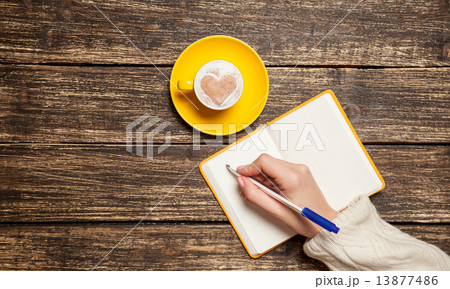 Female hand writing something in notebook near cup of coffee. 13877486