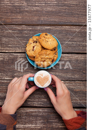 Female hands holding cup of coffee and cookies on wooden table. Female hands holding cup of coffee and cookies on wooden table. 13877977