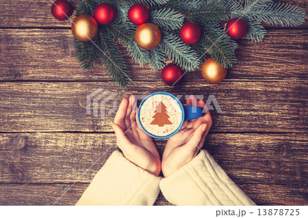 Female holding cup of coffee with cream christmas tree on a tabl Female holding cup of coffee with cream christmas tree on a tabl 13878725