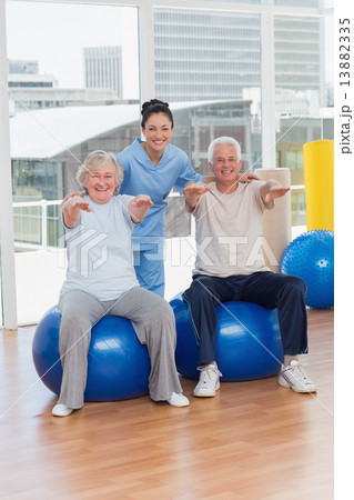 Senior couple on exercis ball with trainer Senior couple on exercis ball with trainer 13882335