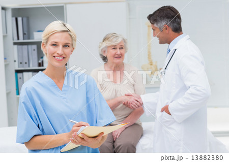 Nurse making reports while doctor and patient shaking hands Nurse making reports while doctor and patient shaking hands 13882380