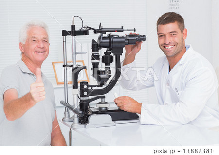 Senior man showing thumbs up while sitting with optician Senior man showing thumbs up while sitting with optician 13882381