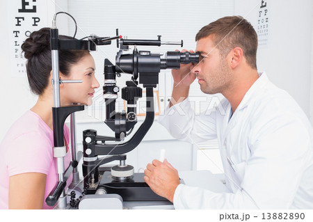 Optician examining womans eyes through slit lamp 13882890