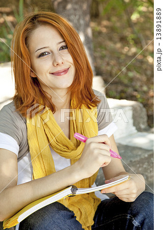 Red-haired student girl with notebook sitting at outdoor. Red-haired student girl with notebook sitting at outdoor. 13891889