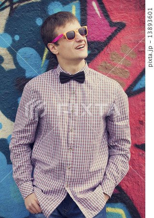 Style teen in glasses standing near graffiti wall. 13893601