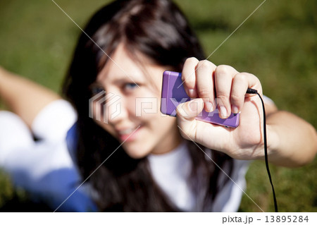 Pretty young brunette girl listening music on green grass in the 13895284
