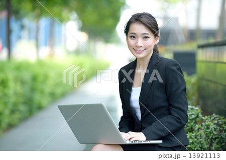 One young successful Chinese businesswoman using laptop sitting along promenade One young successful Chinese businesswoman using laptop sitting along promenade 13921113