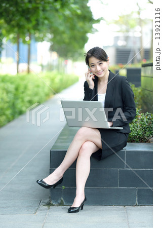 One young successful Chinese businesswoman using mobile phone and laptop sitting along promenade 13921116