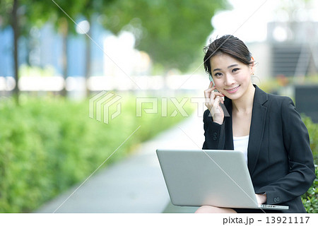 One young successful Chinese businesswoman using mobile phone and laptop sitting along promenade 13921117