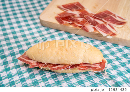 Side view of Serrano ham sandwich over checkered tablecloth 13924426
