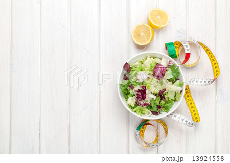 Fresh healthy salad, utensils and tape measure over white wooden Fresh healthy salad, utensils and tape measure over white wooden 13924558