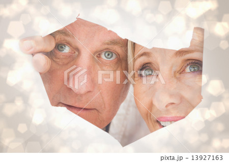 Composite image of older couple looking through rip Composite image of older couple looking through rip 13927163