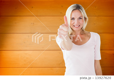 Composite image of happy blonde showing thumbs up and smiling at Composite image of happy blonde showing thumbs up and smiling at 13927620