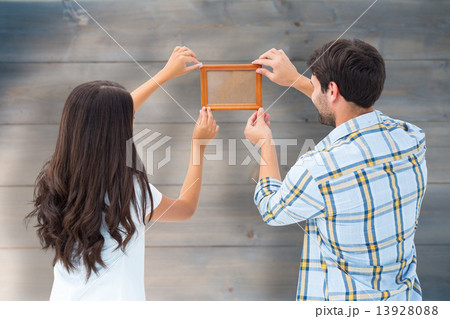 Composite image of happy young couple putting up picture frame Composite image of happy young couple putting up picture frame 13928088