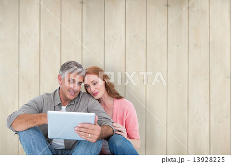 Composite image of casual couple sitting using tablet 13928225