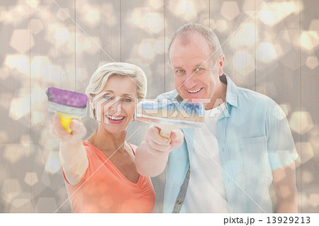 Composite image of happy older couple holding paintbrushes Composite image of happy older couple holding paintbrushes 13929213