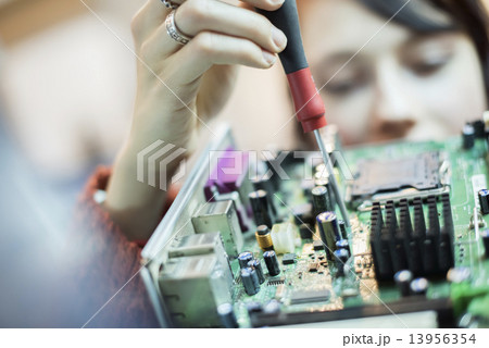 A woman using an electronic screwdriver on a computer circuitboard.  13956354