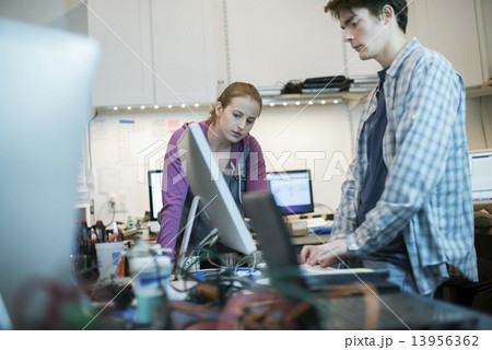 Two people, a man and woman standing at the counter in a computer repair shop.  13956362