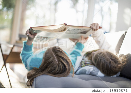 Two girls lying on a sofa on their back, reading a book. Two girls lying on a sofa on their back, reading a book. 13956371