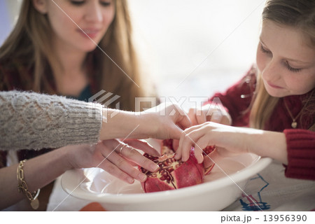 Two girls and a woman sitting at a table, picking kernels from a pomegranate. 13956390