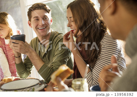A group of people sitting at a table, smiling, eating, drinking and chatting. 13956392