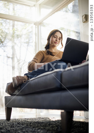 Low angle view of a woman sitting on a sofa looking at her laptop. 13956393