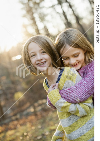 Two smiling girls in a forest, hugging each other. 13956431