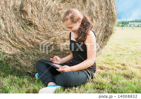Girl with  device siting close  to haystack 14008832
