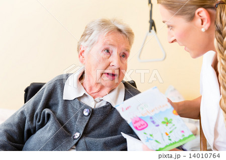 Nurse giving birthday card to senior woman in home Nurse giving birthday card to senior woman in home 14010764