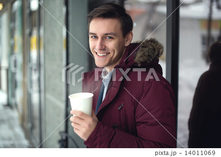Young businessman in a suit and winter coat is drinking hot coffee at cold street with steam bright Young businessman in a suit and winter coat is drinking hot coffee at cold street with steam bright 14011069
