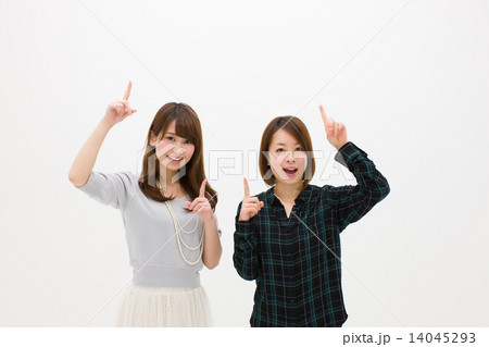 笑顔で上を指差す二人の若い女性の写真素材