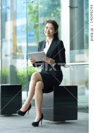 Successful chinese businesswoman using tablet iPad sitting along office promenade Successful chinese businesswoman using tablet iPad sitting along office promenade 14049244