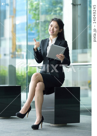 Successful chinese businesswoman giving thumb up gesture using tablet iPad sitting along promenade 14049245