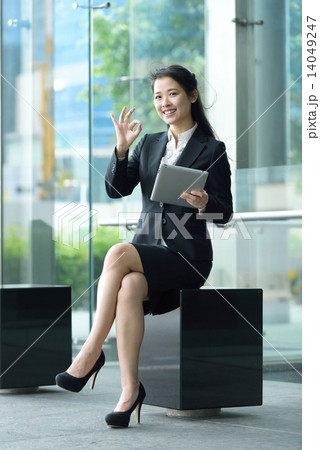Successful chinese businesswoman giving ok gesture using tablet iPad sitting along promenade Successful chinese businesswoman giving ok gesture using tablet iPad sitting along promenade 14049247