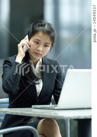 Successful chinese businesswoman using mobile phone and laptop along office promenade Successful chinese businesswoman using mobile phone and laptop along office promenade 14049337