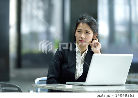 Chinese businesswoman in thoughts while using laptop along office promenade 14049363