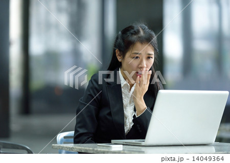 Chinese businesswoman giving an astonished look while using laptop along office promenade 14049364