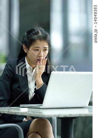 Chinese businesswoman giving an astonished look while using laptop along office promenade 14049365