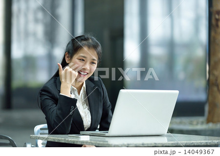 Chinese businesswoman giving thumbs up while using laptop along office promenade 14049367