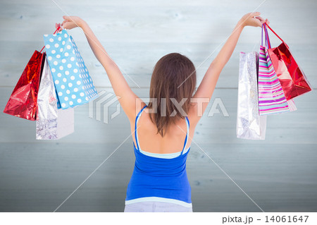 Composite image of rear view of a brunette woman raising shoppin 14061647