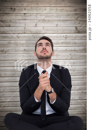 Composite image of businessman sitting praying and looking up 14062058