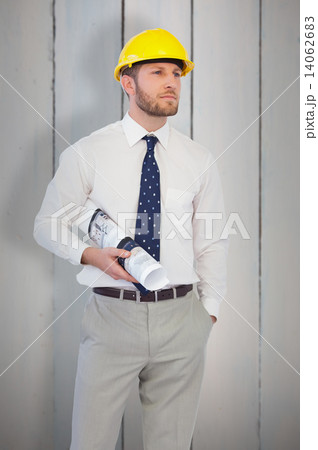 Composite image of young architect posing with hard hat and plan 14062683