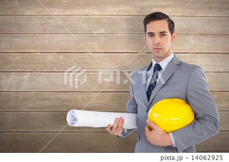 Composite image of serious architect holding plans and hard hat 14062925