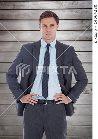Composite image of serious businessman with hands on hips 14064280
