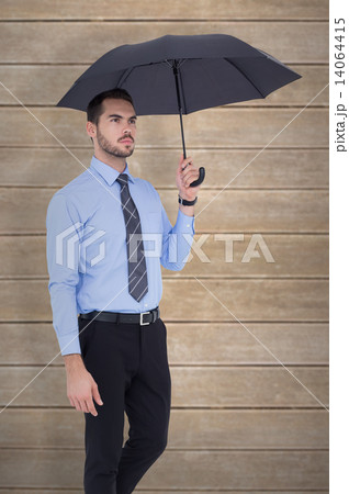 Composite image of serious businessman standing under umbrella Composite image of serious businessman standing under umbrella 14064415