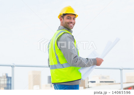 Architect in protective clothing holding blueprint outdoors 14065596
