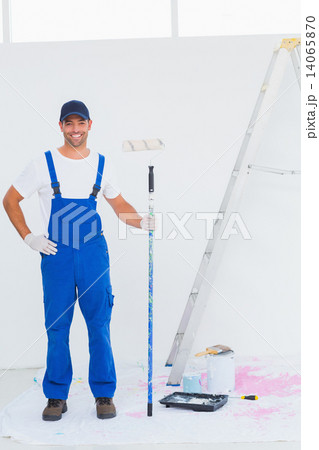 Handyman in overalls holding paint roller at home 14065870